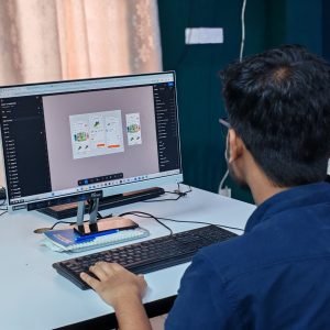 A young designer focused on creating user interfaces on a desktop computer in an office setting.